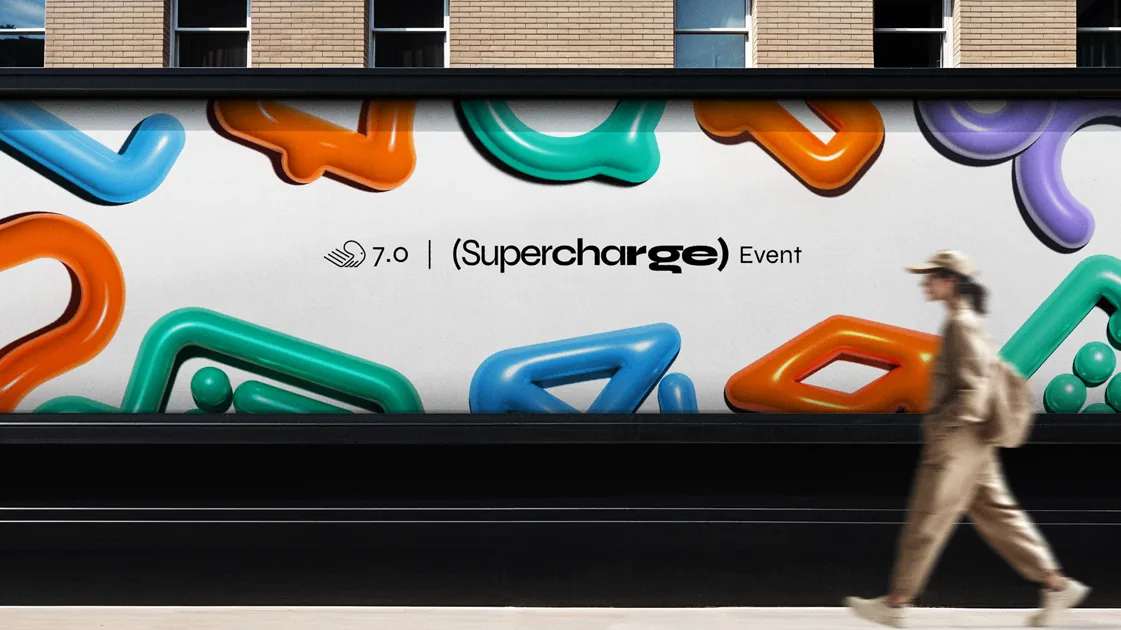 Anúncio em muro de rua: “7.0 | (Supercharge) Event” entre formas 3D infláveis